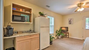 A compact kitchen with a microwave, refrigerator, and coffee maker. There is a window with blinds, a ceiling fan, and a television in the background. - Cozy Studio With Yard, 6 Miles to Dwtn Beaufort! (Beaufort)