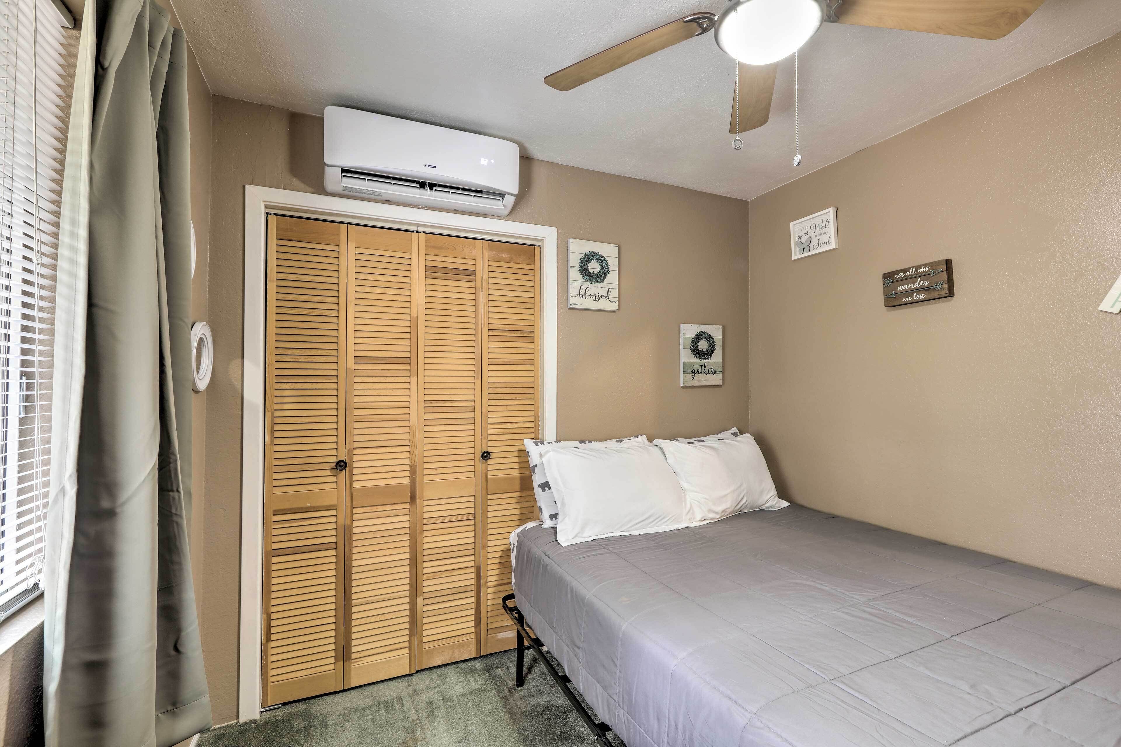 A bedroom with a bed, a ceiling fan, an air conditioning unit, a wooden closet, and wall decorations.