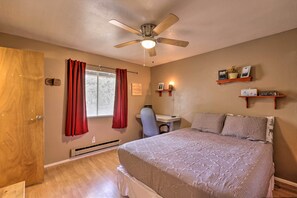 A bedroom with a bed, a desk, a chair, a ceiling fan, and two wall-mounted shelves with decorative items. - Bright Pine Cabin: Direct Trail Access & Deck! (Pine)
