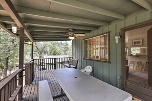A covered outdoor area with a long table and benches, a ceiling fan, and a window with blinds. - Bright Pine Cabin: Direct Trail Access & Deck! (Pine)
