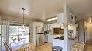 Una cocina moderna con armarios blancos, un refrigerador de acero inoxidable y una mesa de comedor de madera con sillas.