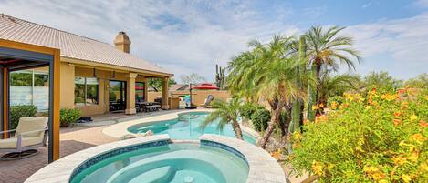 A swimming pool with a hot tub, surrounded by palm trees and cacti, with a covered patio area and outdoor seating.