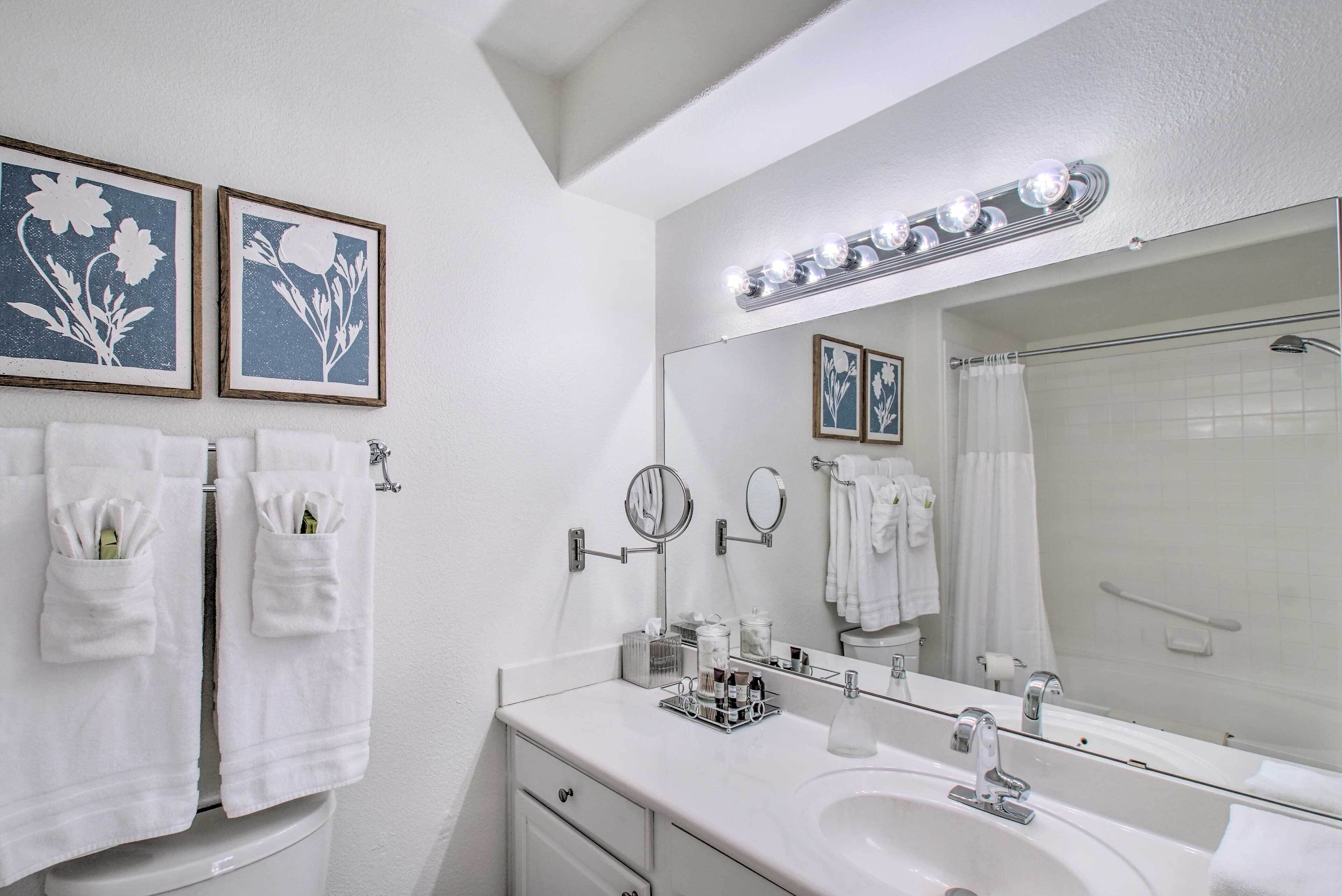 A bathroom with a white sink, two mirrors, a vanity with toiletries, and a shower curtain.