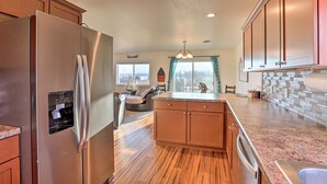 A kitchen with wooden cabinets, a stainless steel refrigerator, a built-in island with a sink, and a view of the outdoors through a window. - Lake Mcconaughy Getaway With Covered Patio (Lewellen)