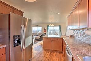 A kitchen with wooden cabinets, a stainless steel refrigerator, a built-in island with a sink, and a view of the outdoors through a window.