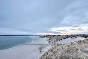 A beach with a clear view of the ocean, a parking area, and a line of trees.