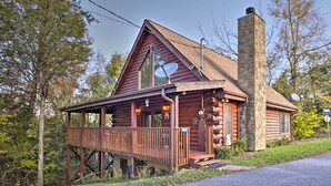Une cabane en rondins avec une cheminée en pierre, une véranda et une antenne parabolique.