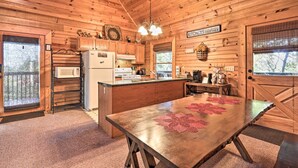 Une cuisine rustique aménagée dans une cabane en bois, avec un îlot central, des placards en bois, un four à micro-ondes, un réfrigérateur et une pancarte sur laquelle on peut lire : « CUISINES SOLIDAIRES ».