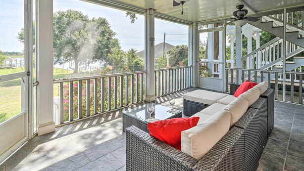 A covered outdoor seating area with wicker furniture and a glass table, overlooking a landscaped area and a staircase. - Waterfront Hampstead Home: Dock & Waterway Access! (Hampstead)