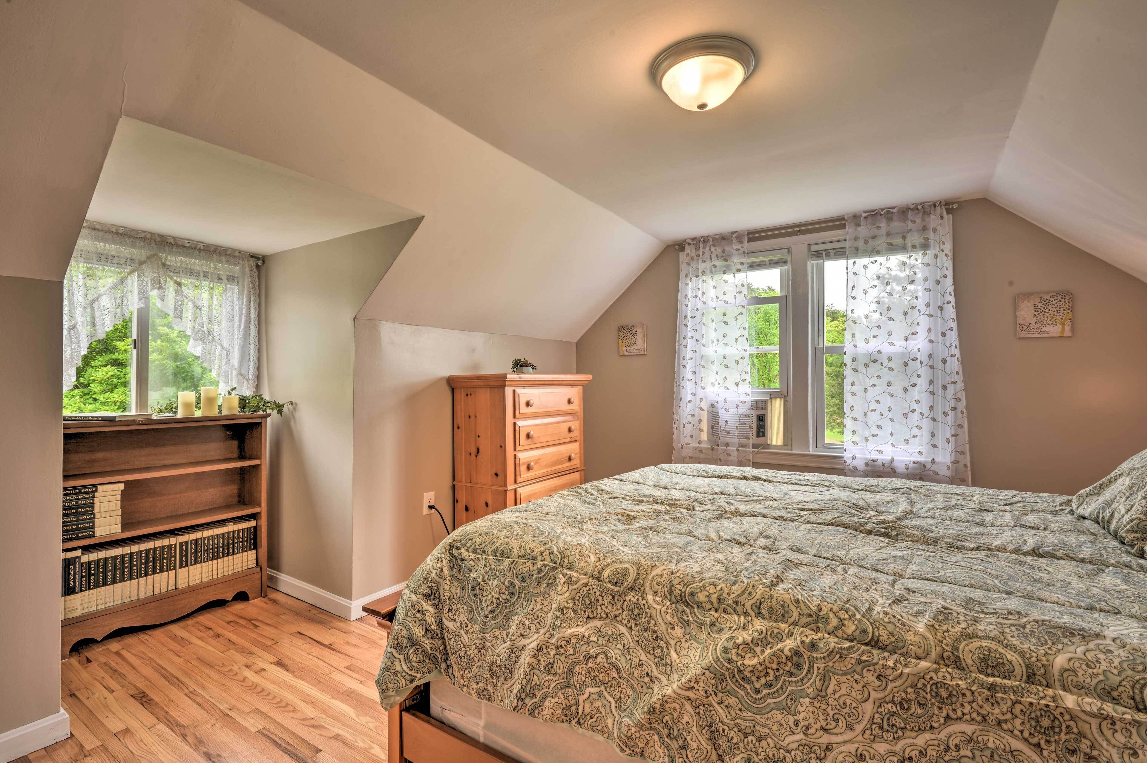 A bedroom with a bed, a wooden dresser, a bookshelf, and a window with curtains.