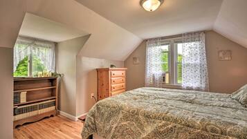A bedroom with a bed, a wooden dresser, a bookshelf, and a window with curtains.