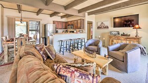 A cozy living room with a large sofa, a wooden coffee table, and a leather armchair. A kitchen with wooden cabinets and a bar area is visible in the background. - Patio & Fireplace: Country Club Pinetop Condo! (Pinetop)