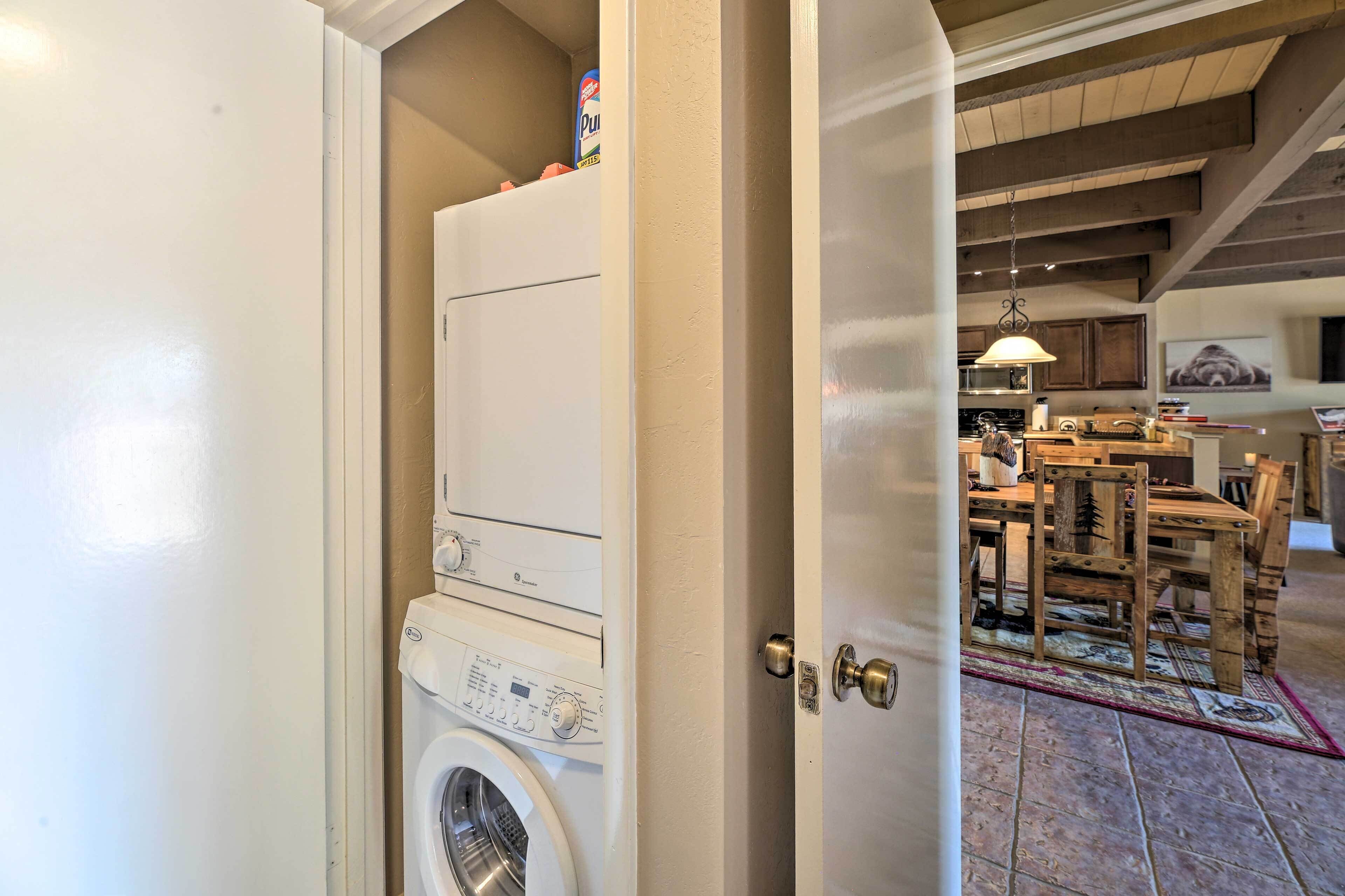 A laundry room with a washing machine and dryer, a wooden dining table with chairs, and a kitchen area visible through an open door.