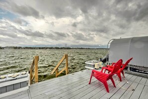 Een houten steiger met rode stoelen en een kleine tafel, met uitzicht op een wateroppervlak onder een bewolkte lucht.