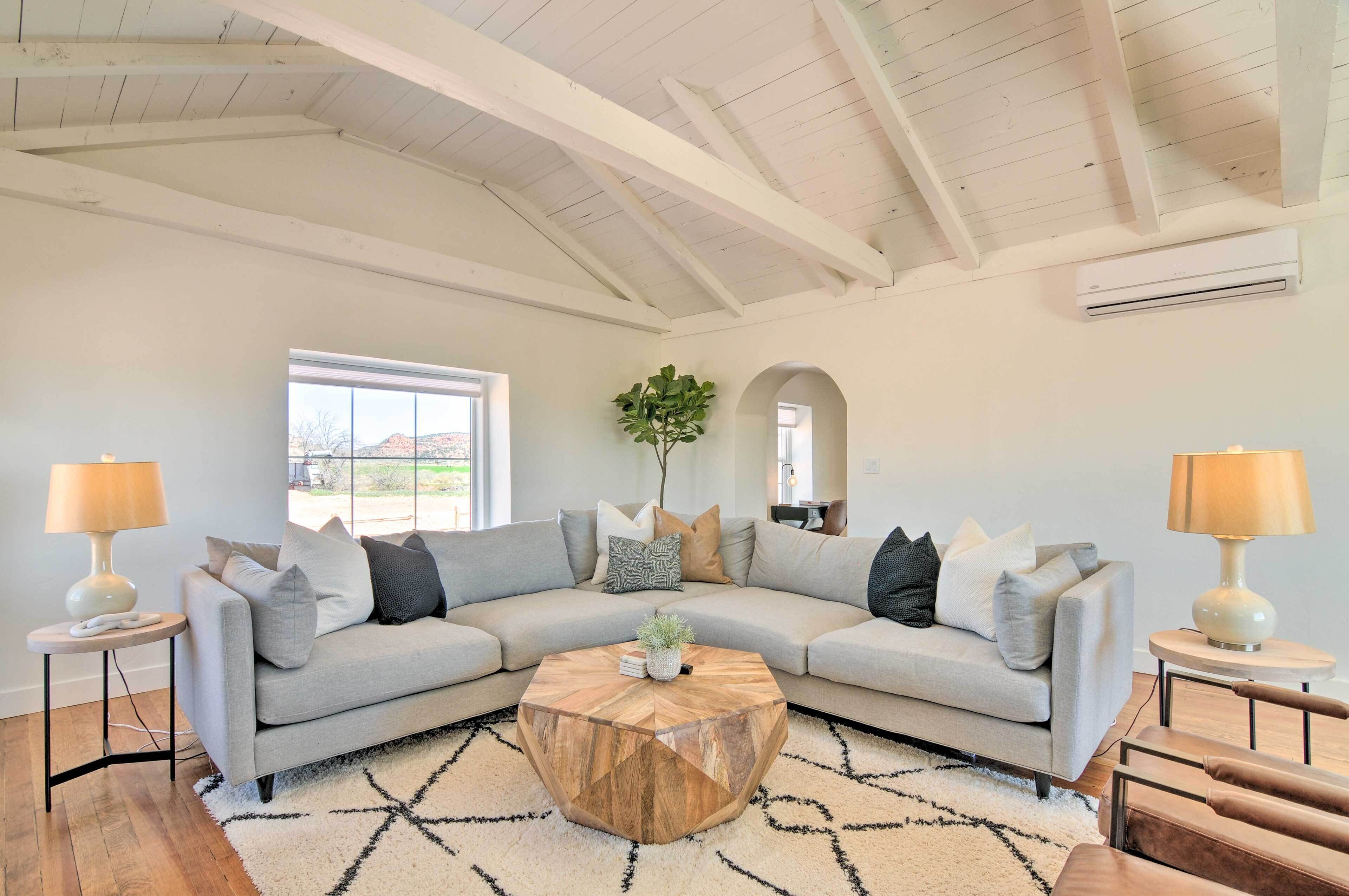 A modern living room with a light grey sectional sofa, a wooden coffee table, and a white ceiling with exposed beams.