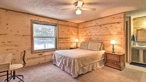 A bedroom with wooden walls, a bed, two bedside tables with lamps, a chair, and a window with a view of trees. - Cozy Crosby Cabin Near Serpent Lake + Main St (Crosby)