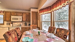 A dining area with a table set for four, surrounded by floral-patterned chairs. A microwave and wooden cabinets are visible in the background. - Cozy Crosby Cabin Near Serpent Lake + Main St (Crosby)