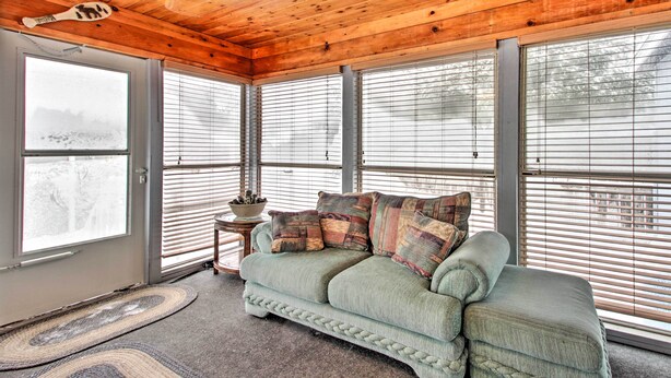 A cozy room with a wooden ceiling, a green sofa with patterned cushions, and large windows with blinds. - Cozy Crosby Cabin Near Serpent Lake + Main St (Crosby)