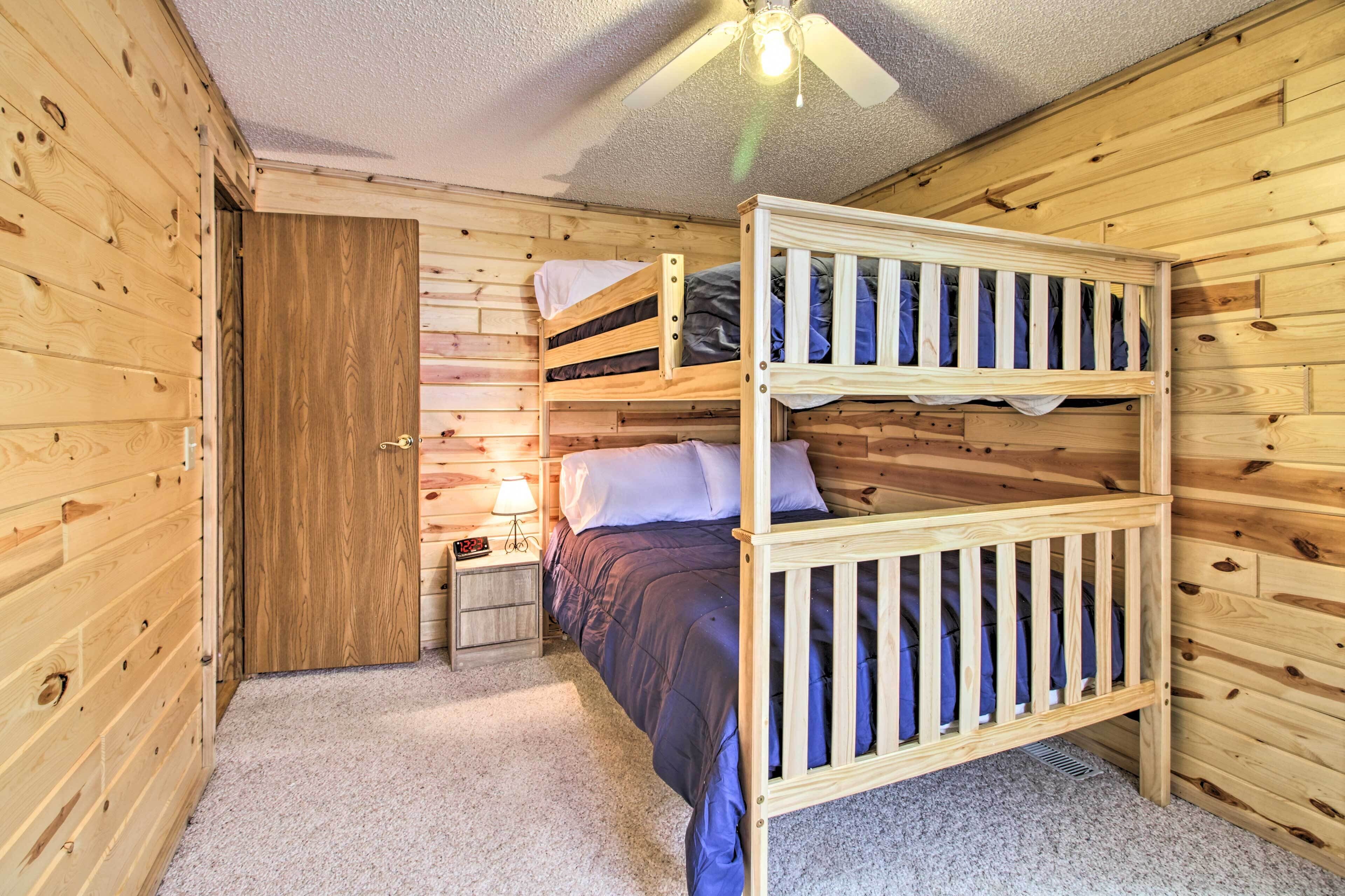 A wooden cabin room with bunk beds, a ceiling fan, and a nightstand with a lamp.