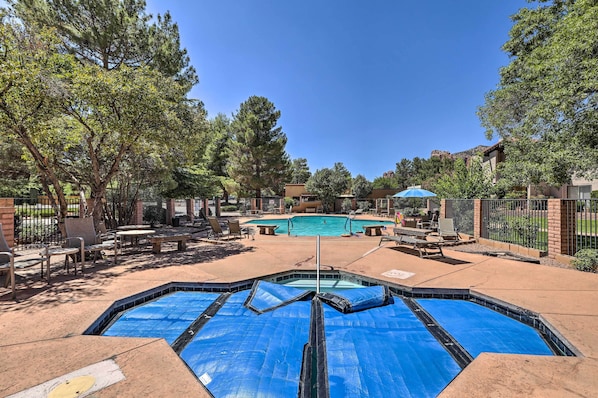 A swimming pool area with a hot tub, lounge chairs, and a covered seating area.