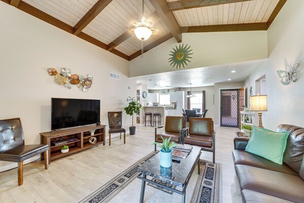 A spacious living room with a large flat-screen TV, leather sofas, a coffee table, and a dining area in the background.