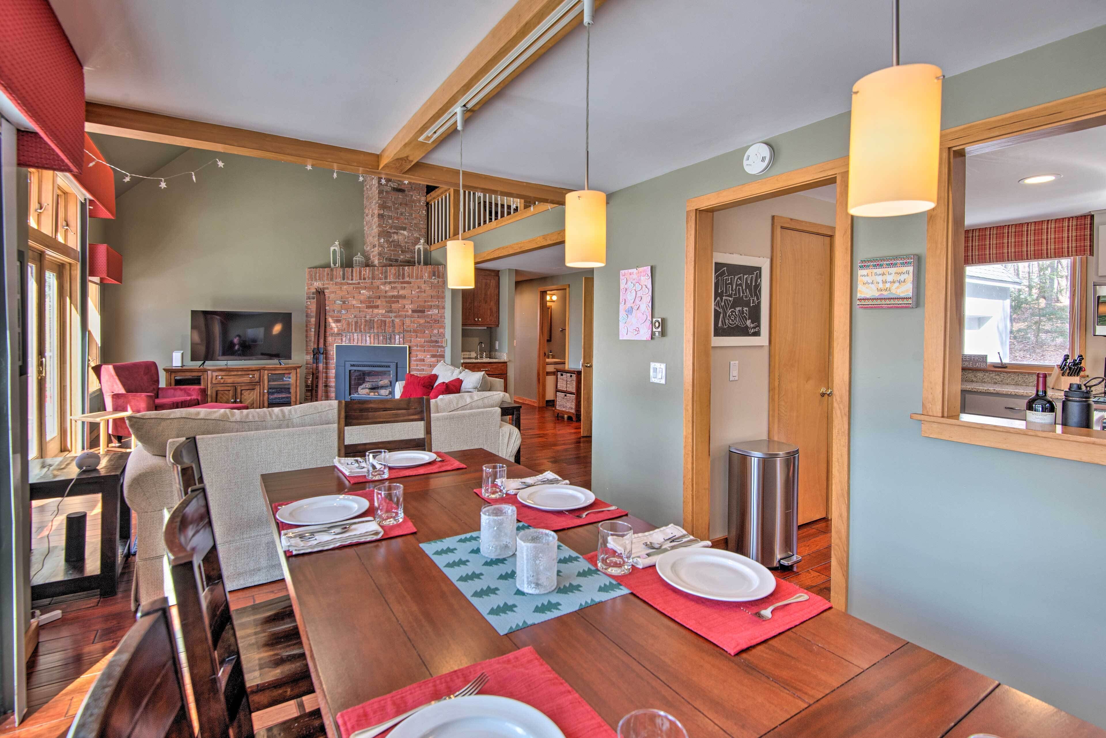 A dining area with a wooden table set for four, a brick fireplace, and a television in the background.