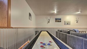 A shuffleboard table with pucks in various colors, a wooden bar on the left, and a grey couch on the right. - 6 Mi to Big Sky Resort! Group Retreat w/ Mtn Views (Big Sky)
