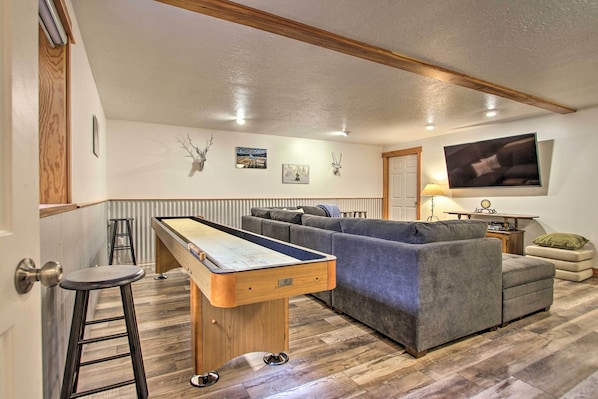 A living room with a pool table, grey sofa, and a television mounted on the wall.