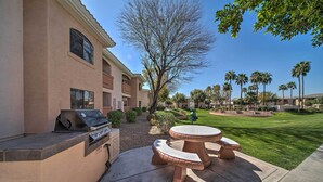 An outdoor patio with a grill, seating, and a well-maintained lawn with palm trees. - Bright Phoenix Condo - 3 Mi to State Farm Stadium! (Phoenix)