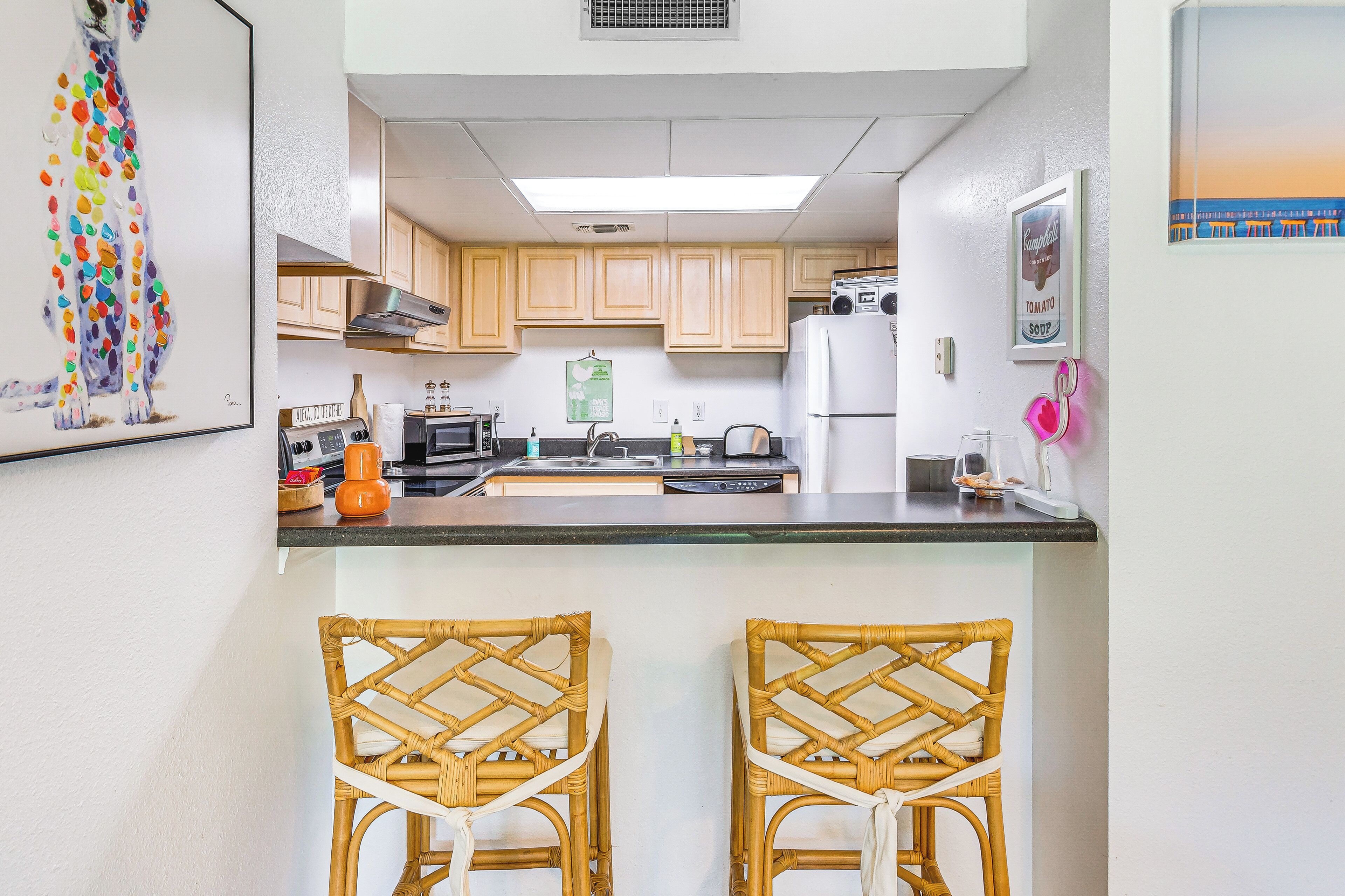A kitchen with wooden cabinets, a refrigerator, a microwave, and a sink. There are two wicker chairs at the counter.