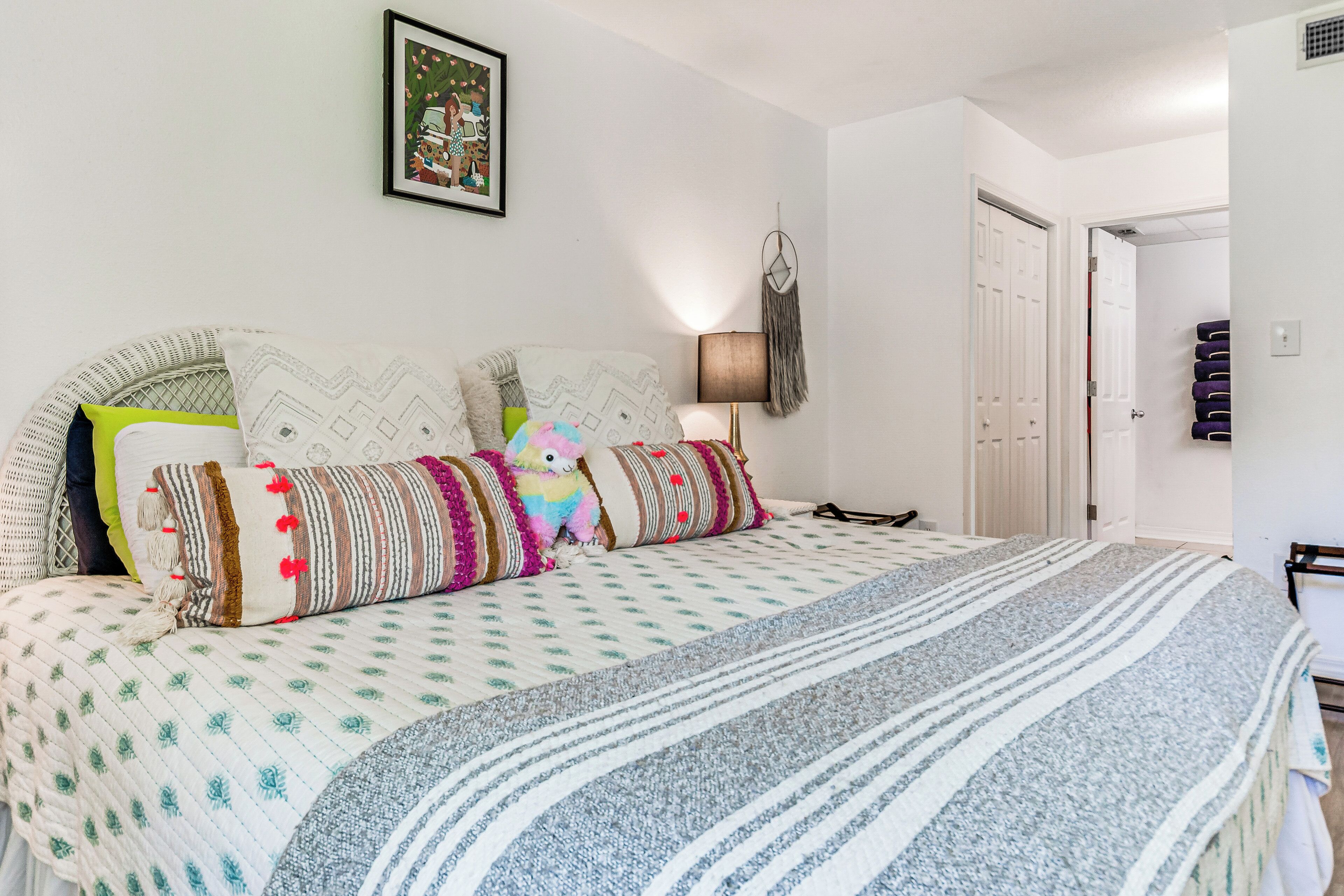 A neatly made bed with patterned bedding and pillows, a wall-mounted dreamcatcher, and a framed picture above the bed.
