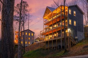 Un immeuble à plusieurs étages doté d’un balcon, entouré d’arbres et illuminé par le ciel au coucher du soleil.
