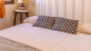Een slaapkamer met een wit hoofdeinde, een bed met een geborduurd sprei en twee aan de muur bevestigde bloemschilderijen.