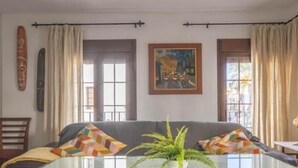 Una sala de estar con sofá, cojines estampados, un cuadro y una planta.