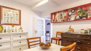 Comedor con una mesa blanca, sillas de madera, un mueble de madera con frascos, y una pared decorada con varios cuadros y carteles.
