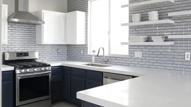A modern kitchen with a brick backsplash, white cabinetry, a stainless steel stove, and a window with built-in shelves. -  Luxury Oasis Near the Las Vegas Strip – Sleeps Large Groups in Style (Las Vegas)