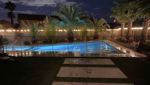 A swimming pool with a glass enclosure, surrounded by palm trees and a fence. -  Luxury Oasis Near the Las Vegas Strip – Sleeps Large Groups in Style (Las Vegas)