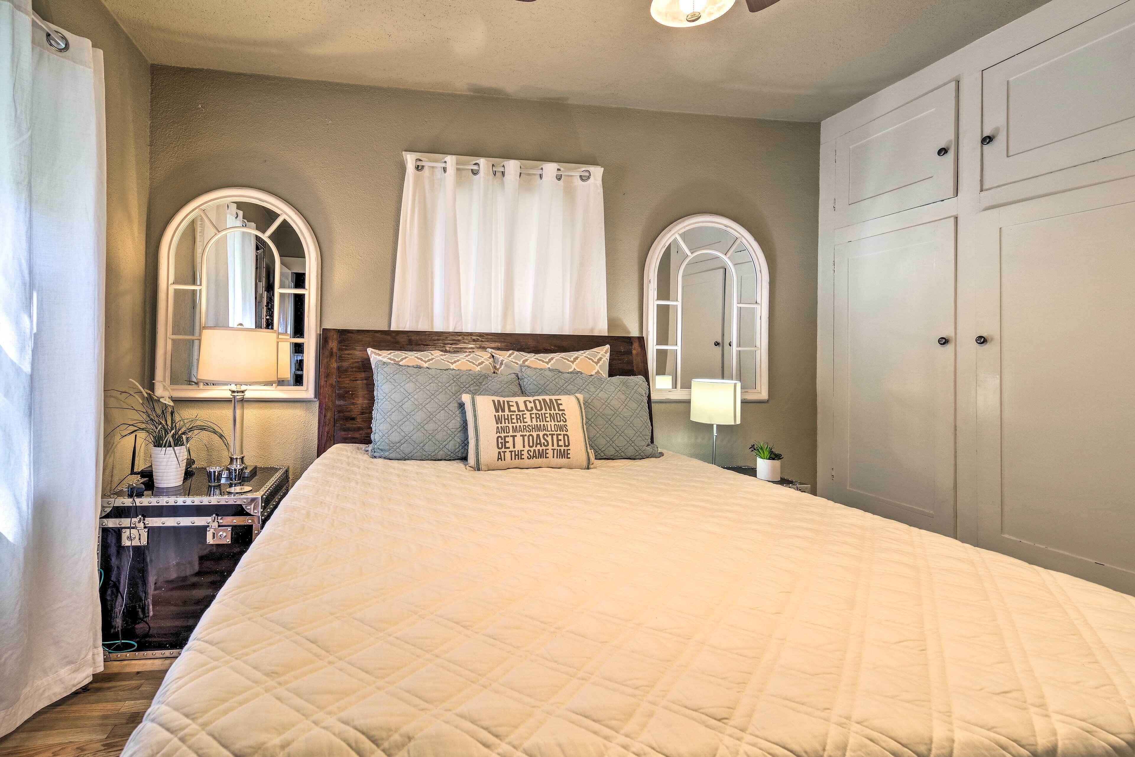 A bedroom with a large bed, two bedside tables with lamps, a nightstand, a wardrobe, and a window with curtains.