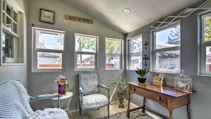 Habitación acogedora con pared gris, un escritorio de madera, una silla, una mesita con un florero y una ventana con vistas al exterior.