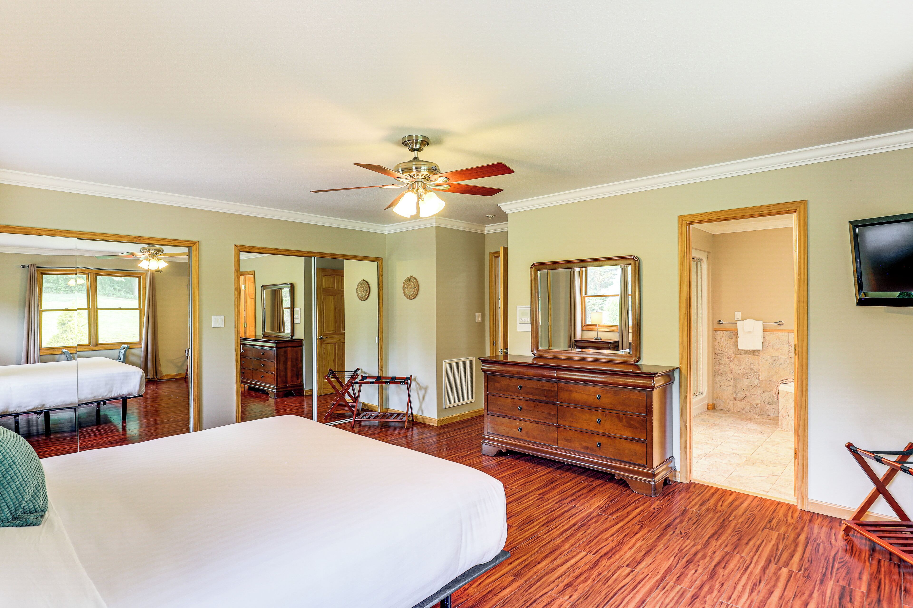 A hotel room with a large bed, a dresser, a ceiling fan, a television, and a bathroom visible through an open door.
