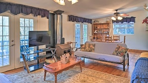 A cozy living room with a fireplace, a sofa, a TV, and a ceiling fan. - Secluded Bryson City Home w/ Deck, Steps to Creek! (Bryson City)