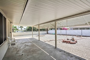 Uma área externa coberta com piso de concreto, uma cadeira de plástico branca e um braseiro de tijolos.
