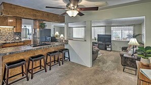 A modern kitchen with a bar area, a ceiling fan, and a living room with a TV and seating. - Restful Riverfront Retreat w/ Private Dock + Patio (Bullhead City)