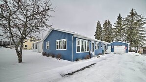 A blue house with a garage, surrounded by snow-covered ground and trees. - Cozy Houghton Lake Heights Cottage w/ Private Yard (Houghton Lake)