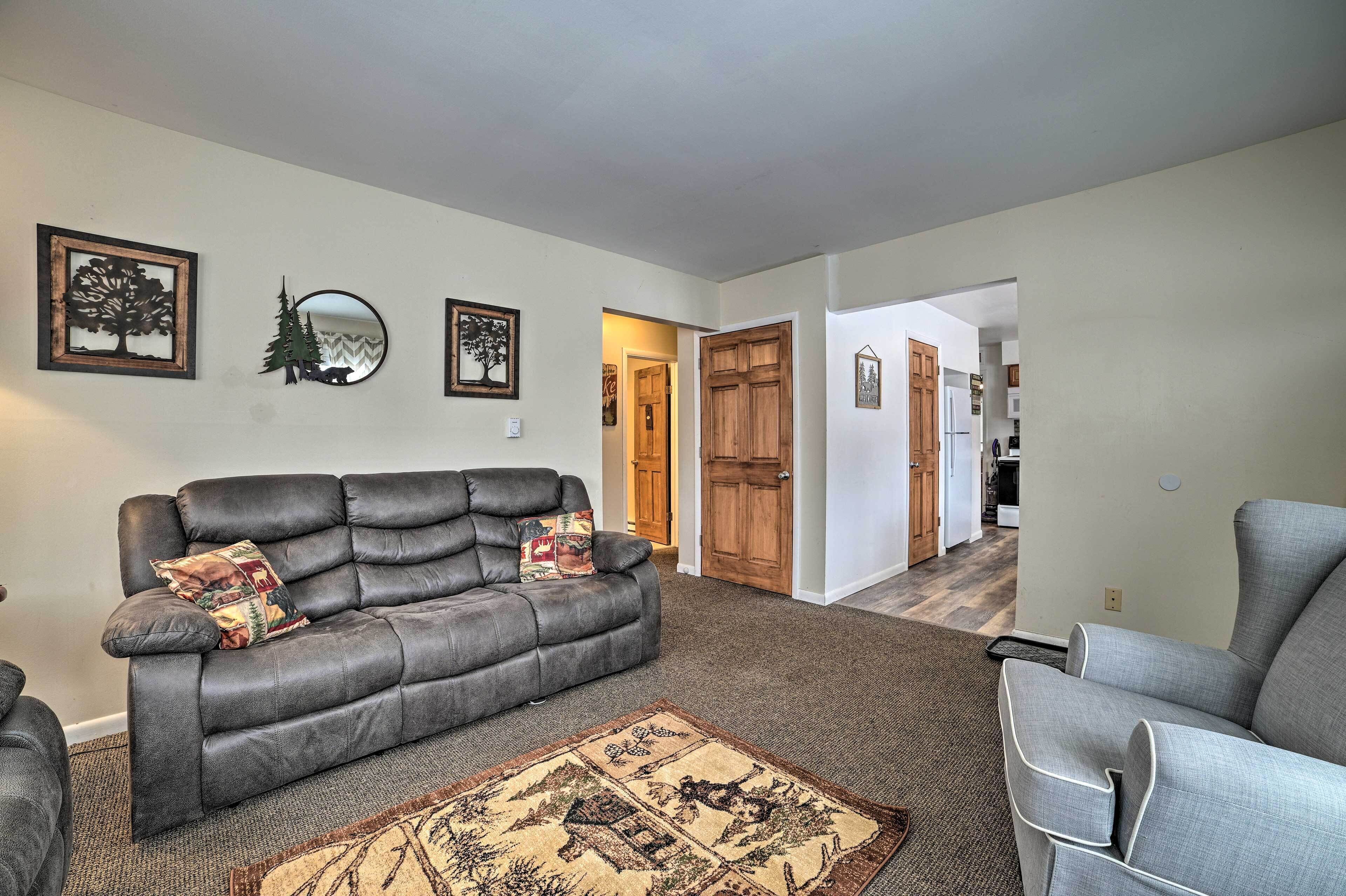 A living room with a grey leather sofa, a patterned rug, and framed wall art.