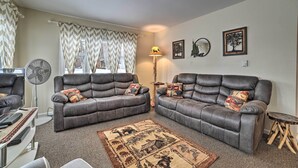 A living room with two leather sofas, a patterned rug, a standing fan, and a small wooden table. - Cozy Houghton Lake Heights Cottage w/ Private Yard (Houghton Lake)