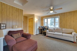 Una sala de estar con un sillón marrón, un sofá blanco y un ventilador de techo.