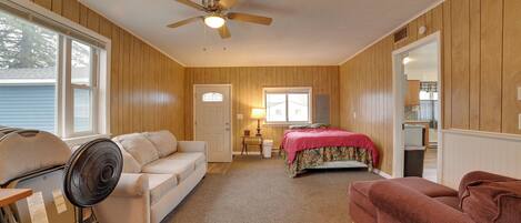 A room with a ceiling fan, a bed with a red blanket, a white couch, and a red couch.