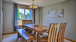 A dining area with a wooden table and benches, a chandelier, a window with curtains, and a wall-mounted painting. - Peaceful, Pet-friendly Washougal Paradise! (Washougal)