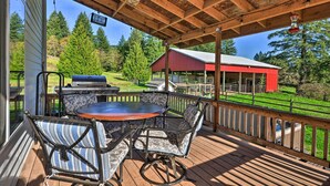 A covered outdoor deck with a grill and seating area, overlooking a red barn and green landscape. - Peaceful, Pet-friendly Washougal Paradise! (Washougal)
